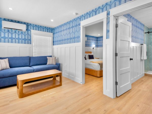 Cozy living area with a blue sofa, wooden coffee table, paneled walls, and a hallway leading to a bedroom and bathroom&mdash;bright, airy, and tidy.